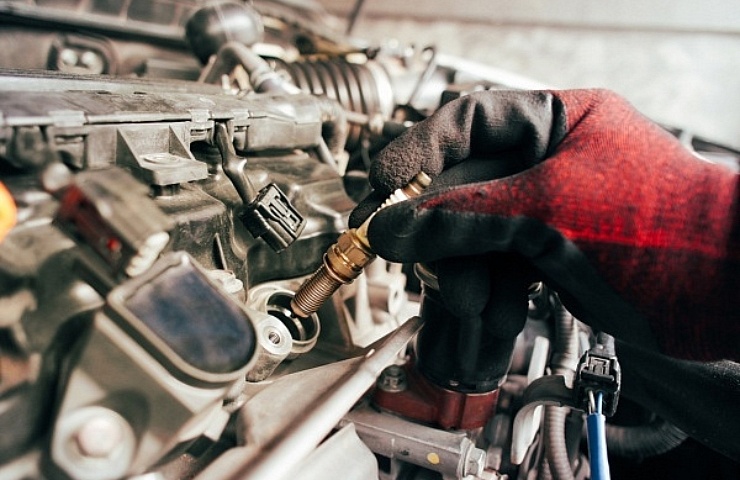 Auto mechanic wearing a read and black glove, replacing a spark plug