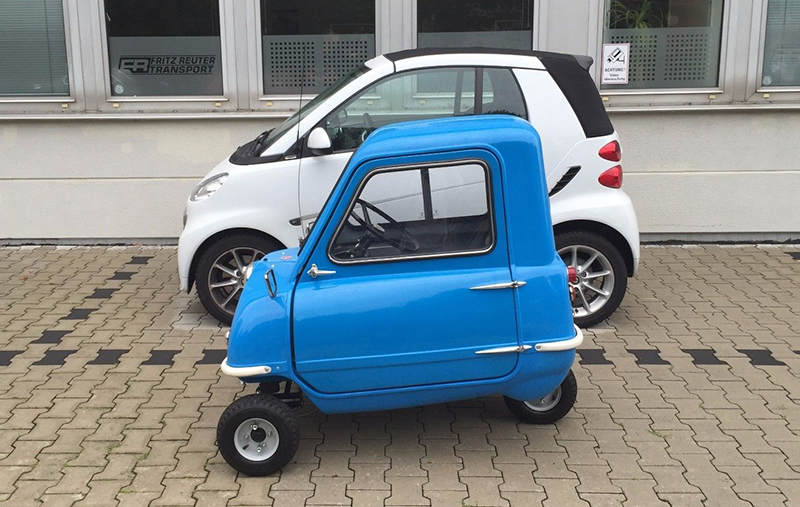 A Peel P50 sitting next to a Smart car