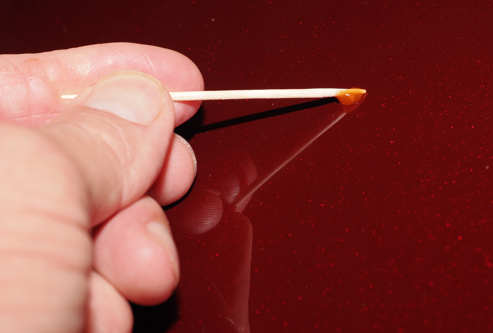 Photo of hand car paint repair by applying paint to a scratch a drop at a time using a toothpick.