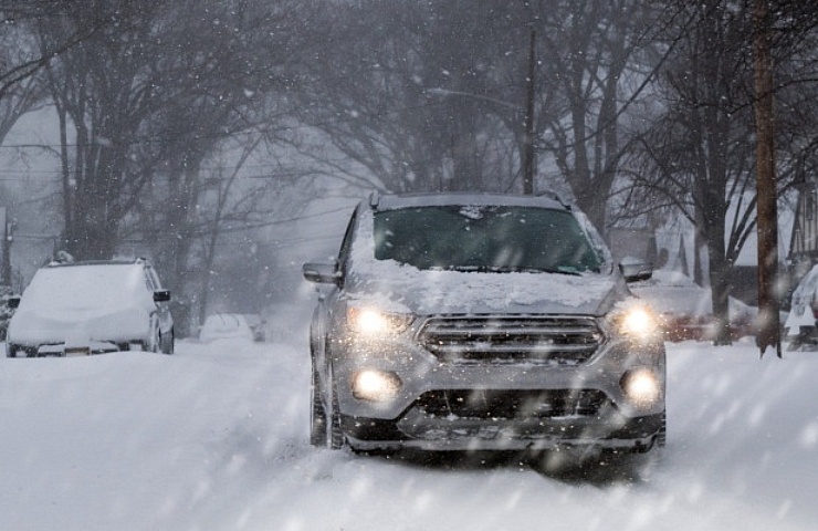 A small SUV driving with low beam headlamps on suburban street a blizzard.