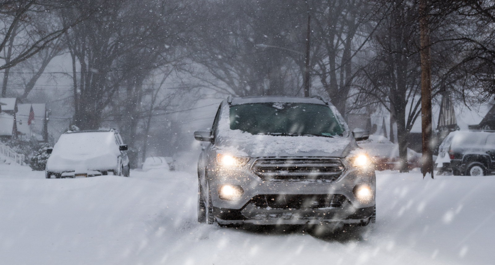 A small SUV driving with low beam headlamps on suburban street a blizzard.
