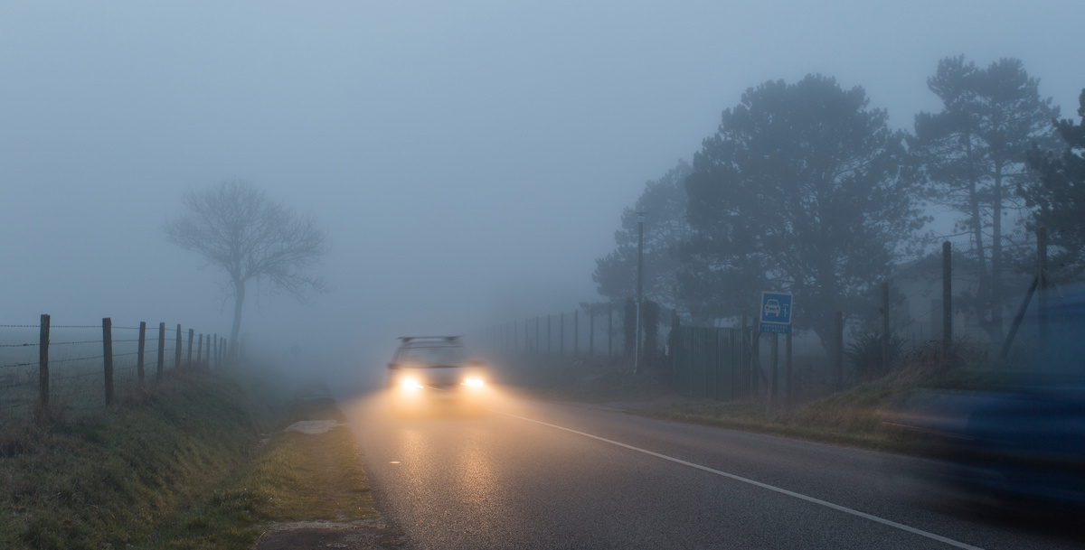 Car driving with low beam headlights on a foggy evening.