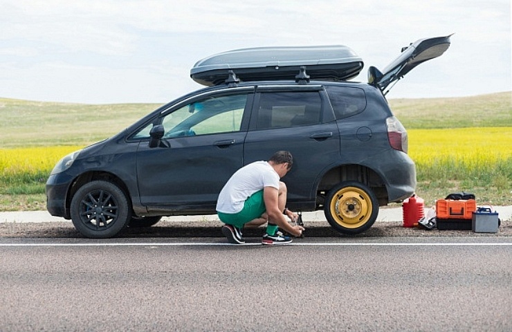 A man changes a tire on a car on the side of the road