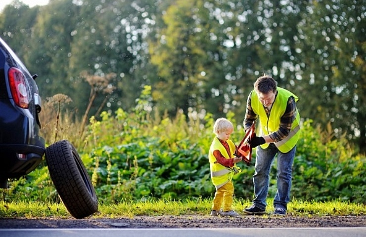 Father and son wearing reflective vests, placing a reflective triangle before changing a tire.