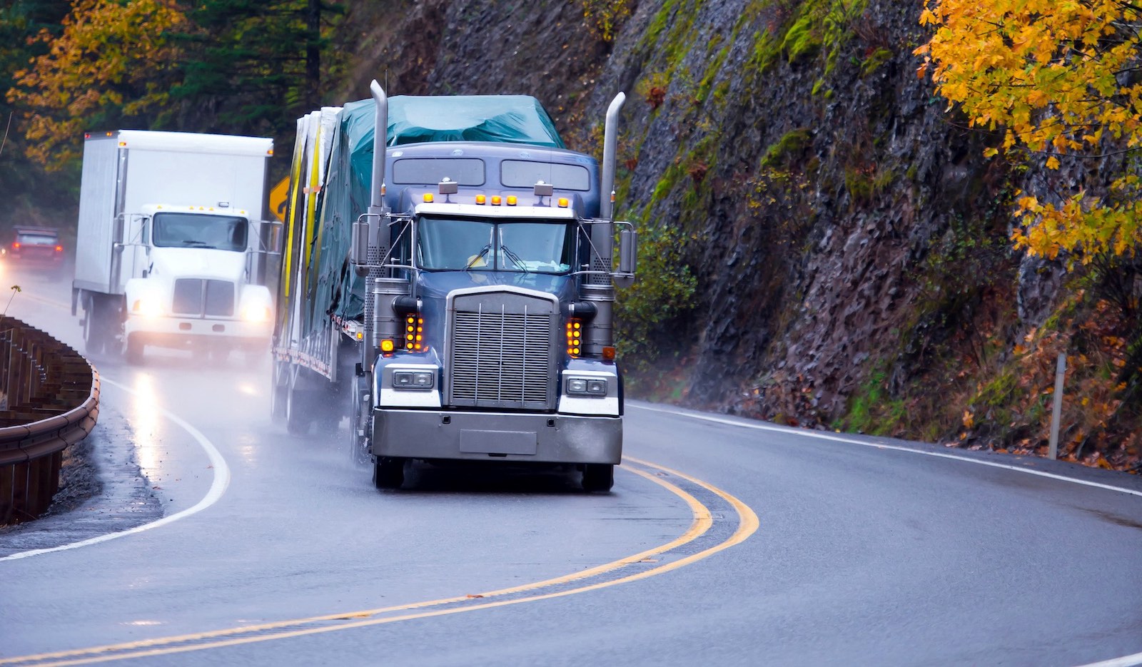Two tractor trailers driving downhill I the autumn rain.