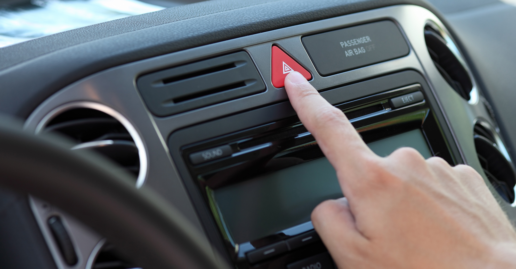 A finger presses the hazard light button, symbolized by a red triangle