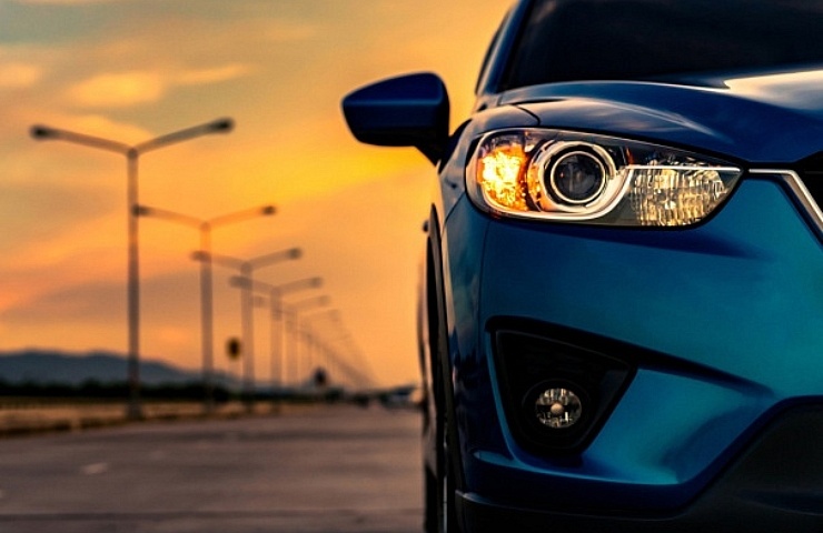 Blue compact SUV car open headlamp light parked on concrete road near the mountain at sunset