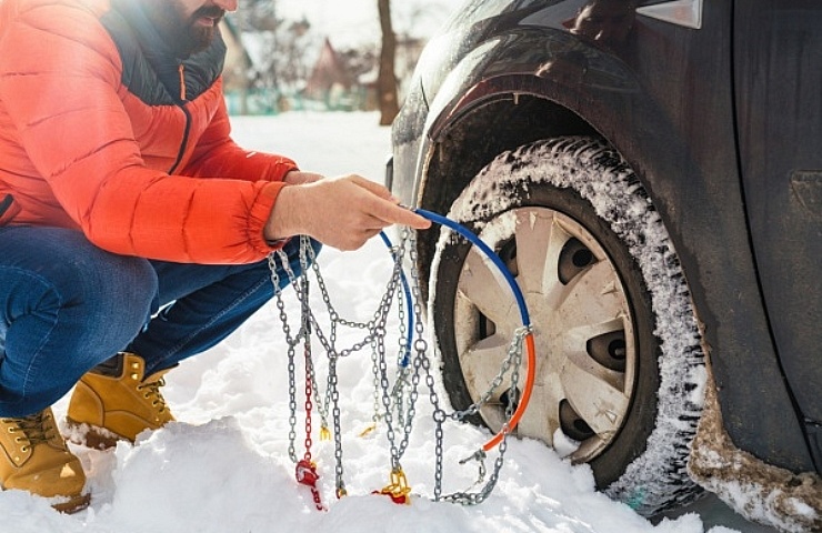 A man puts snow chains on a car tire