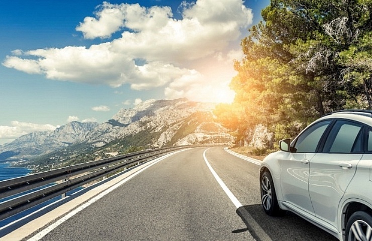 White sedan driving along ocean with mountains