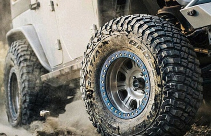 A Jeep kicking up dirt and rocks with BF Goodrich KM3 Mud-Terrain tires.