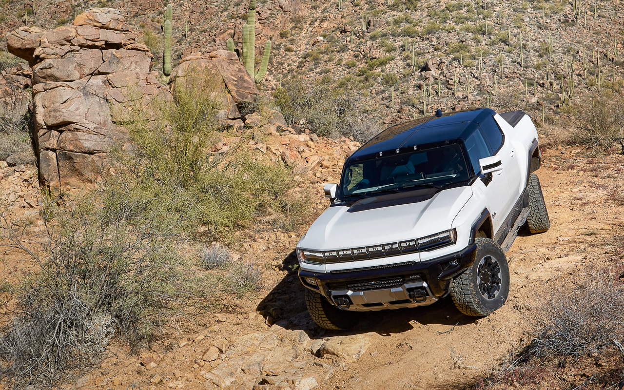 A 2022 GMC Hummer EV pickup moving slowly down a rocky desert slope in CrabWalk four-wheel-steering mode.