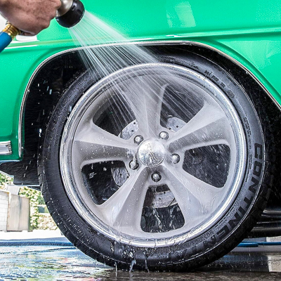 A man rinsing off a custom car wheel with a spray hose