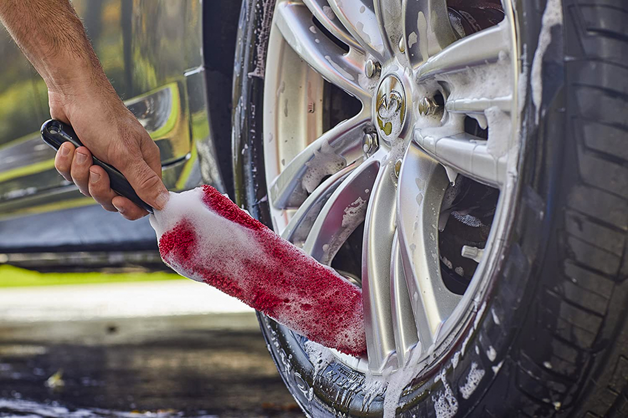 A man cleaning a car wheel with soapy water and a wheel brush