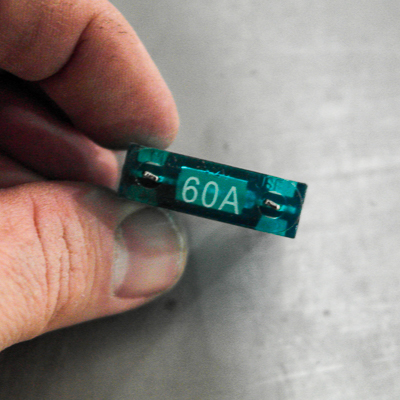 A man's hand holding onto a green 60-AMP MAXI fuse 