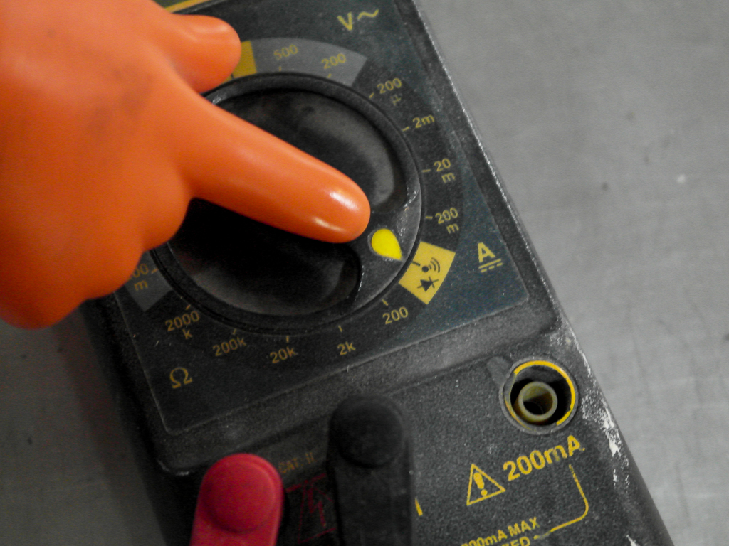 A hand-shaped finger pointer aimed at the continuity setting on a DMM digital multimeter.