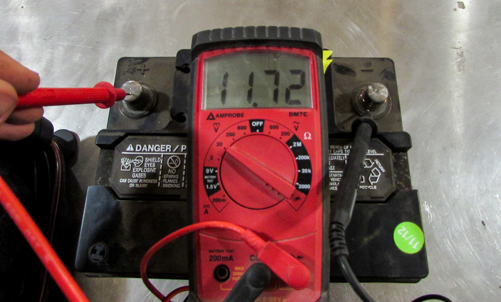 A digital multimeter displaying an 11.72 volt reading of an automotive battery 