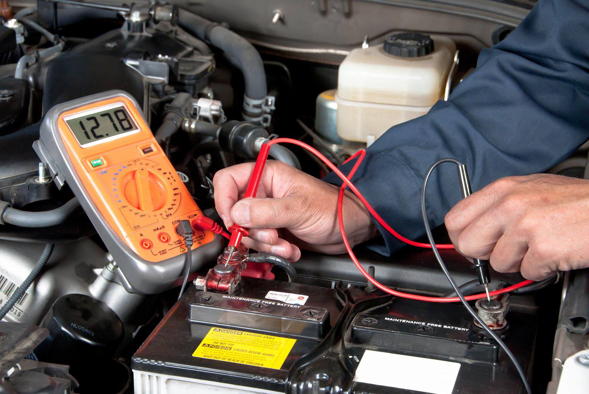A mechanic using a digital multimeter to check car battery voltage