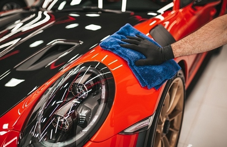 Wiping down a red Porsche with a blue plush microfiber towel.