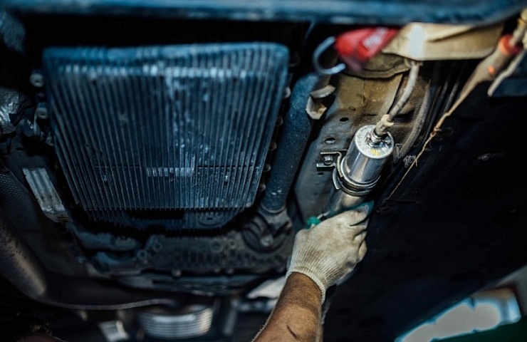 Mechanic servicing fuel filter under car - featured
