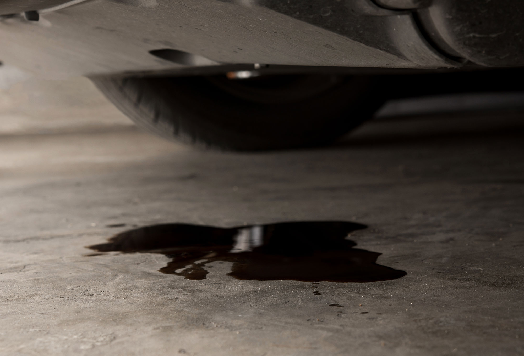 A puddle of oil on a concrete floor under a car engine.