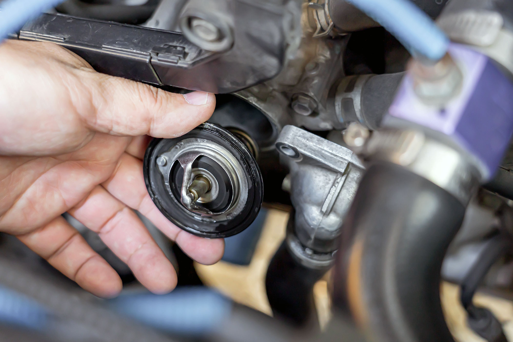 A technician handles an engine thermostat, close-up of hand