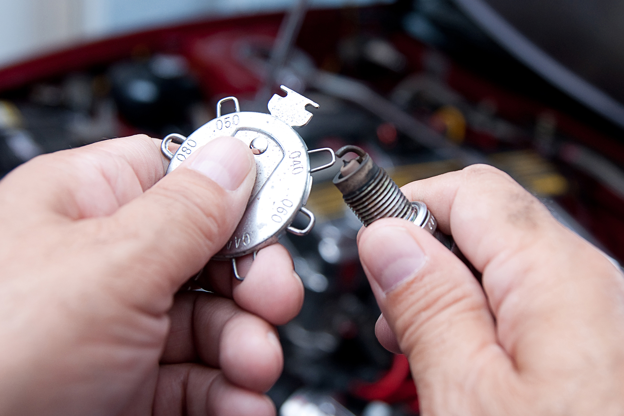 A mechanic gaps a spark plug with a wire-type keychain plug gap tool