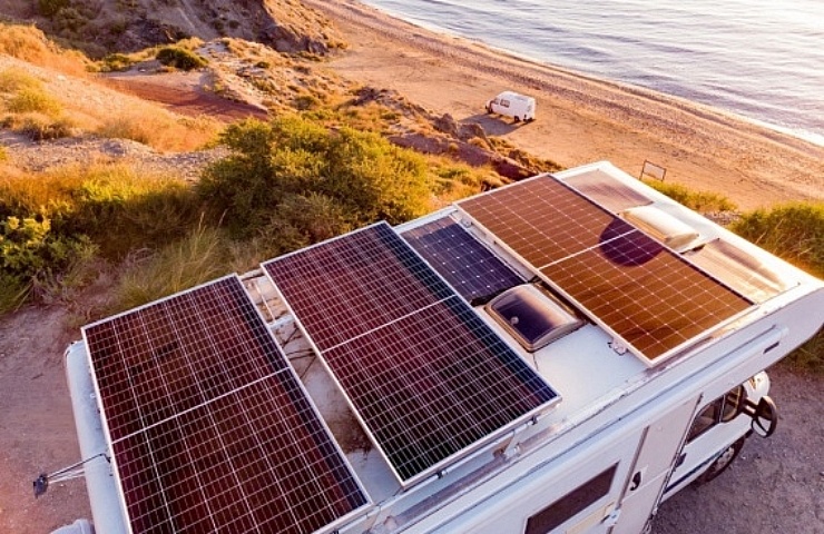 RV with solar panels on roof powering the campsite, parked on cliff overlooking the water.