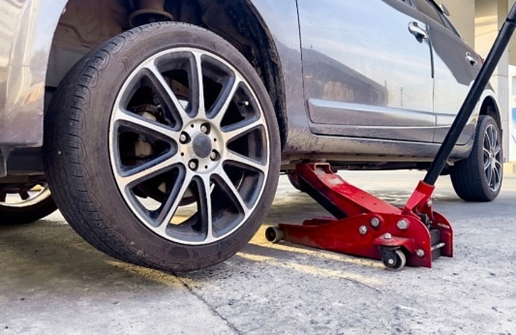 Silver car lifted with red hydraulic floor jack