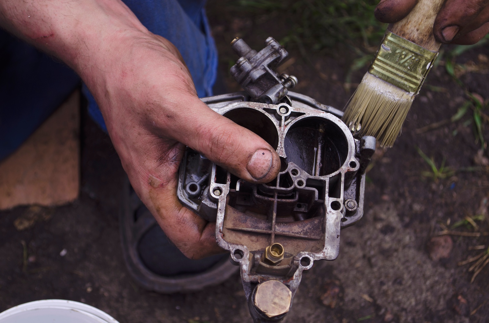 Mechanic cleaning a carburetor with a brush after soaking the unit in solvent.