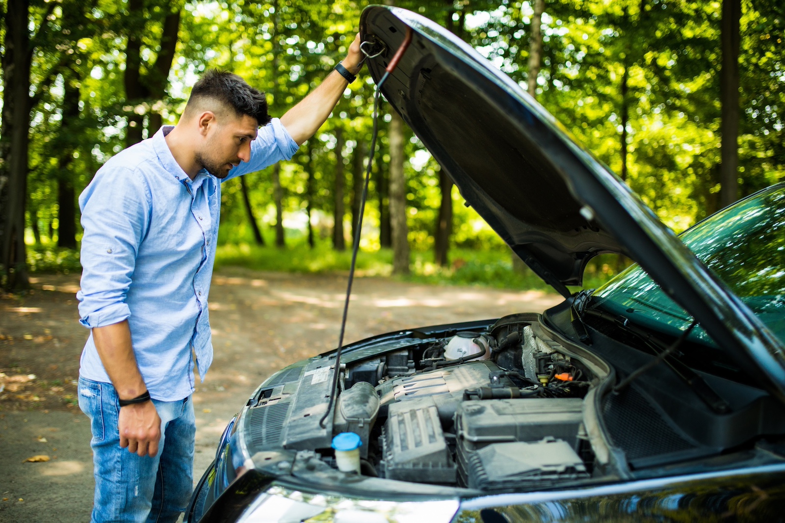 A young man looking at the engine in his broken-down car with disgust.