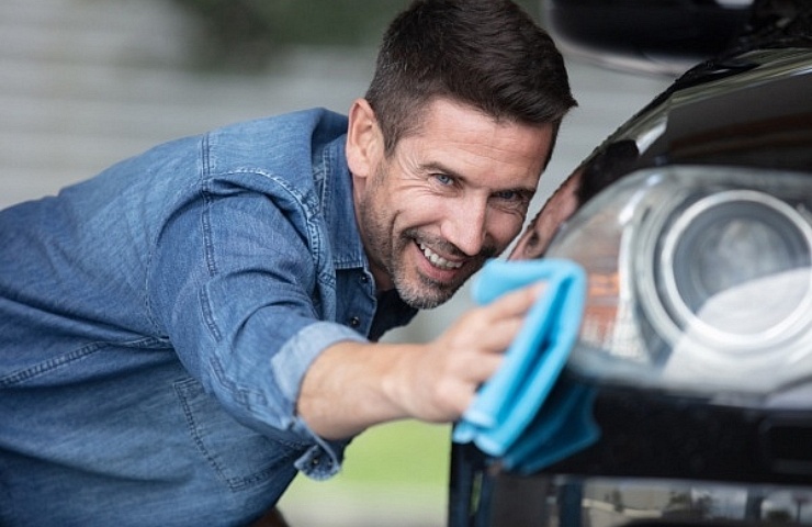 Happy guy cleaning his car's front bumper with a blue microfiber towel.