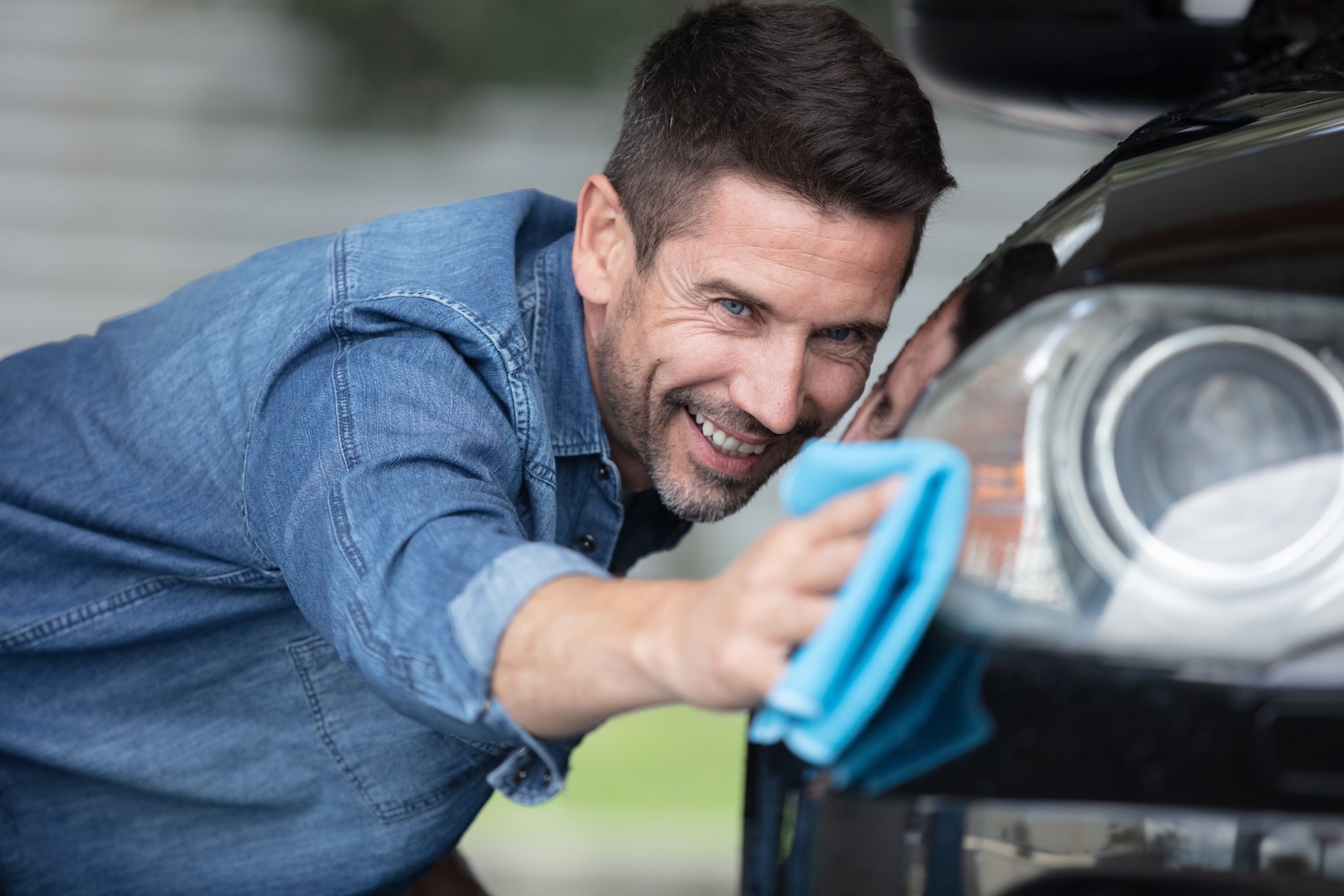 Happy guy cleaning his car's front bumper with a blue microfiber towel.