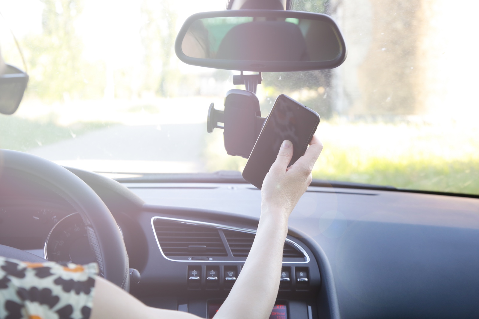 Driver placing a smartphone in a rearview mirror phone mount.