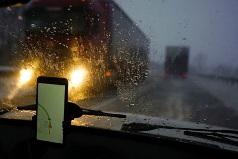 Smartphone displaying navigation information in a phone mount on a rainy evening on the highway with an oncoming tractor. trailers