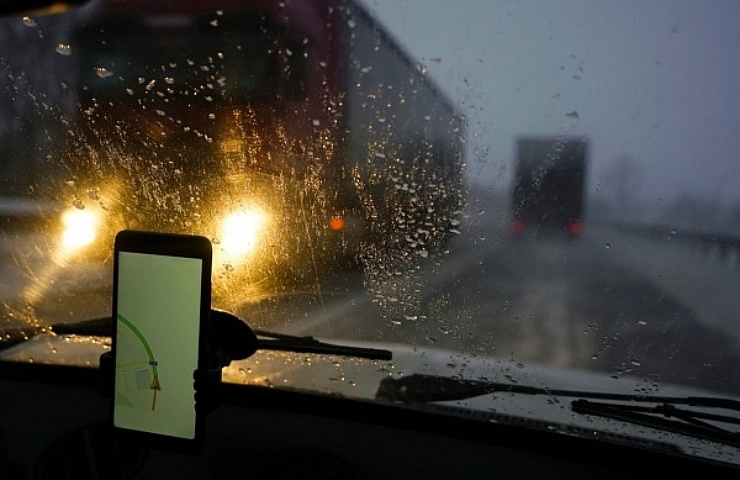 Smartphone displaying navigation information in a phone mount on a rainy evening on the highway with an oncoming tractor. trailers