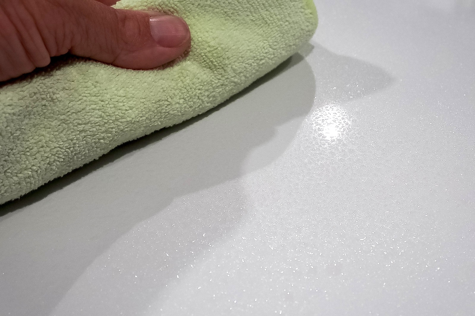 Wiping waterless car wash spray droplets off the surface of a vehicle with white metallic paint using a light green microfiber towel.