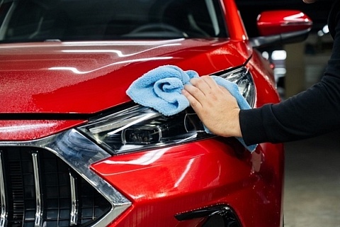 A man wipes down a red car with a microfiber cloth after applying spray wax.