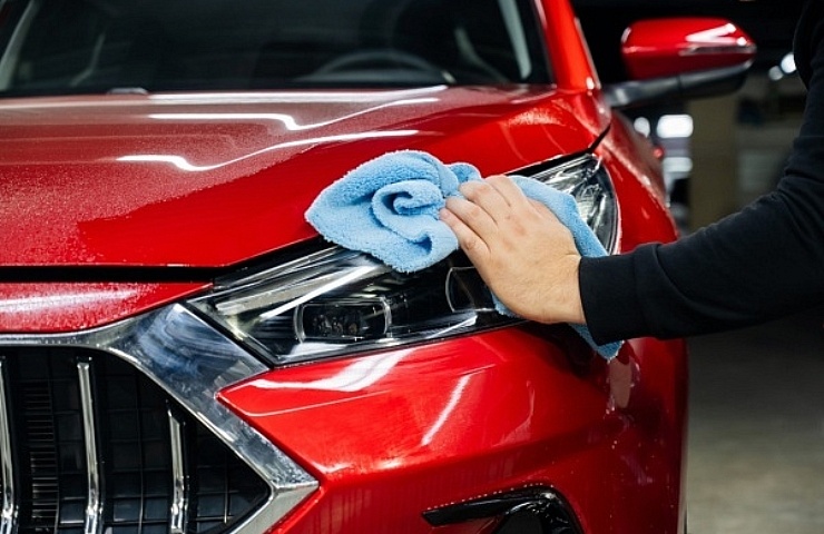 A man wipes down a red car with a microfiber cloth after applying spray wax.