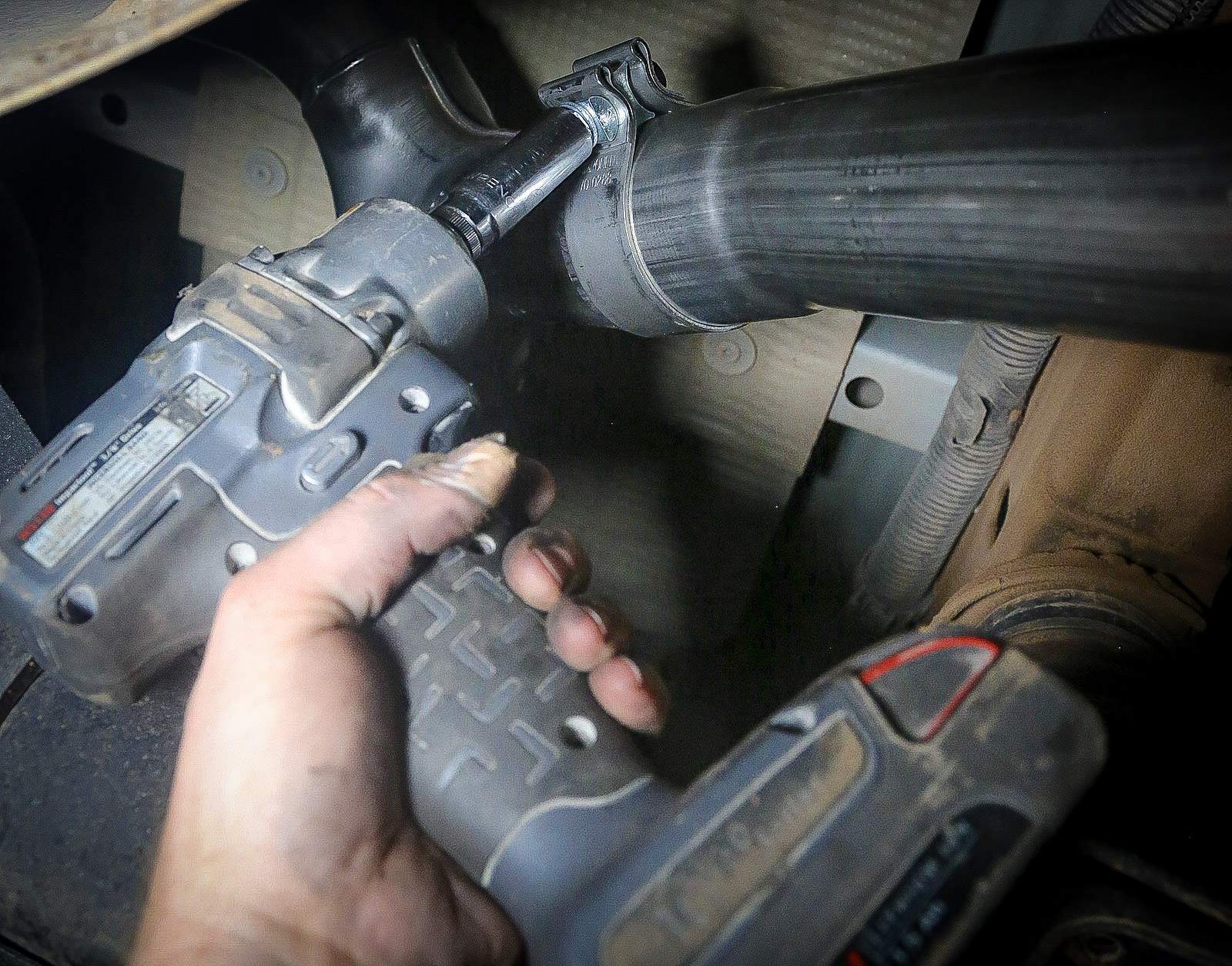 A mechanic tightening a band clamp on a new cat-back exhaust with an electric socket driver.