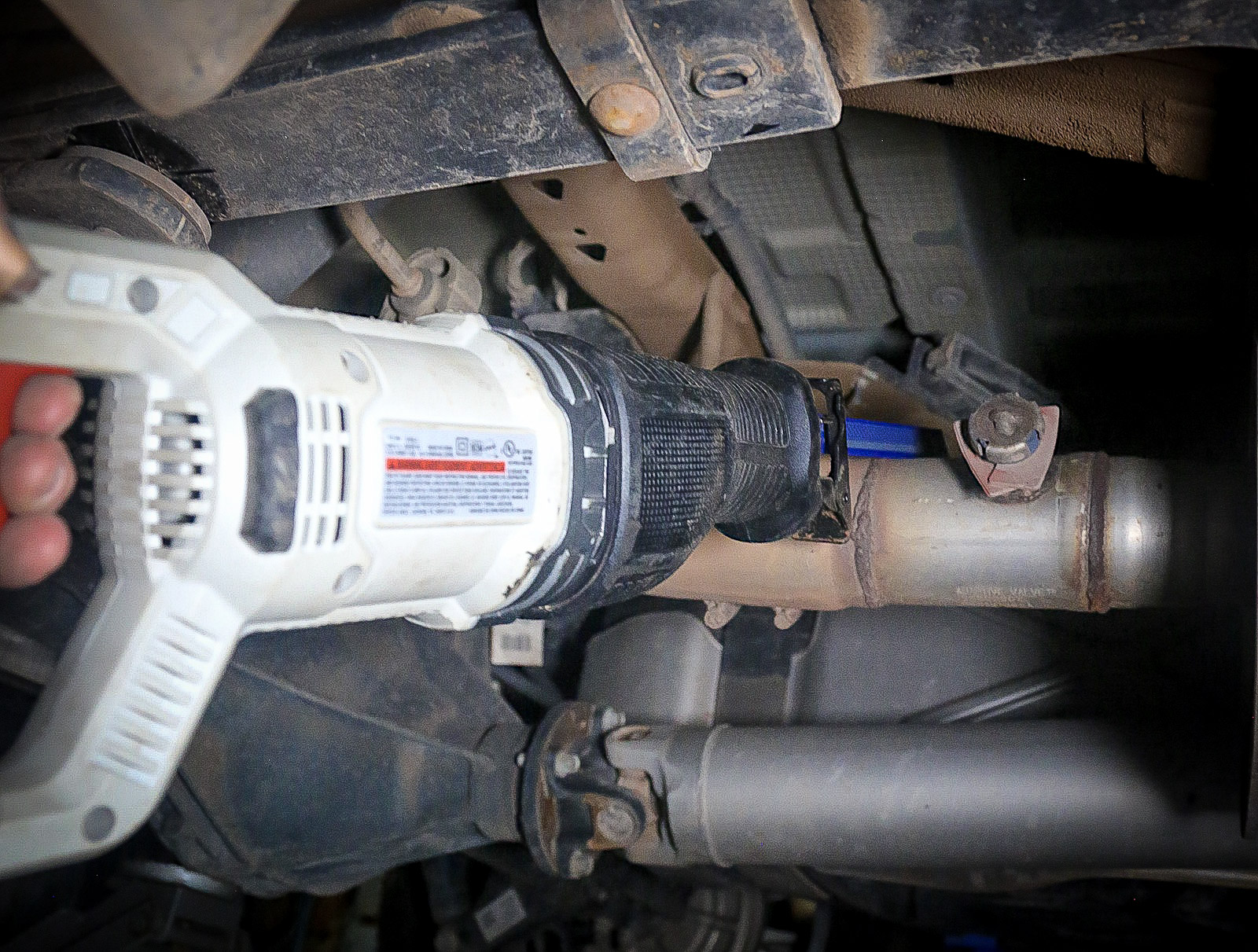 A mechanic cutting the stock exhaust pipe with a reciprocating saw.