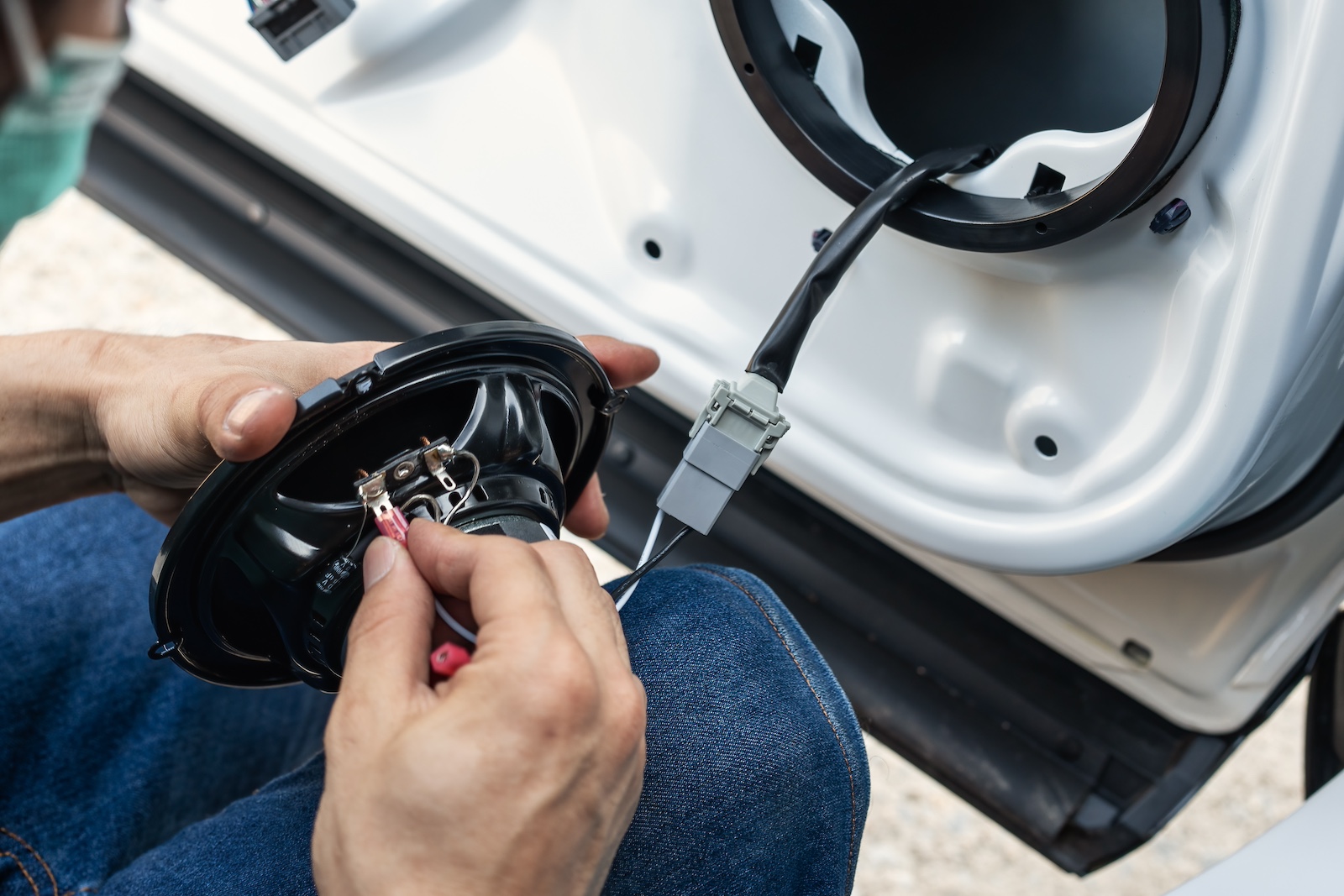 A technician connecting speaker wire to a car speaker.