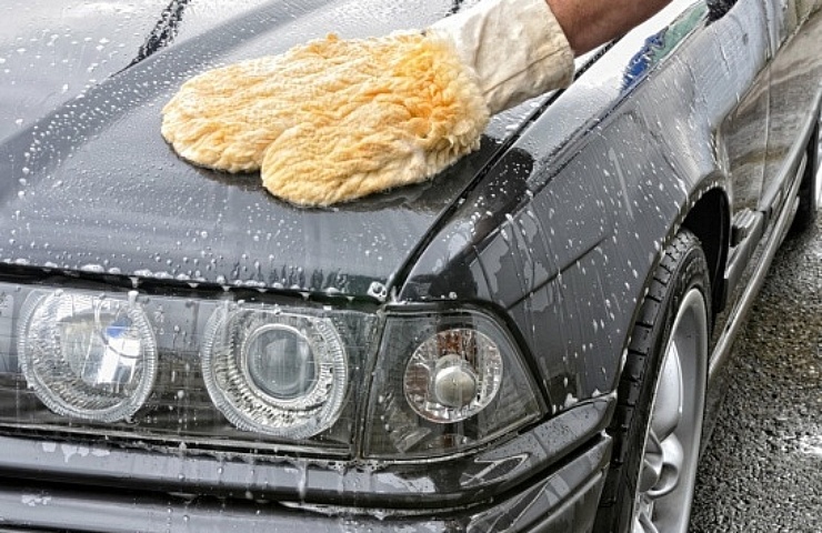 Man using a lambs wool wash mitt to wash a black car.