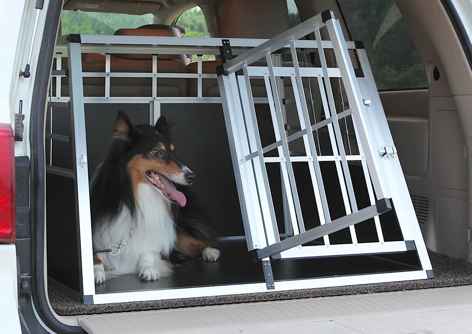 A collie in a metal travel crate in the back of an SUV.