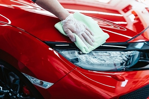 An automotive enthusiast wearing a nitrile glove, wiping down a red car with a microfiber towel.