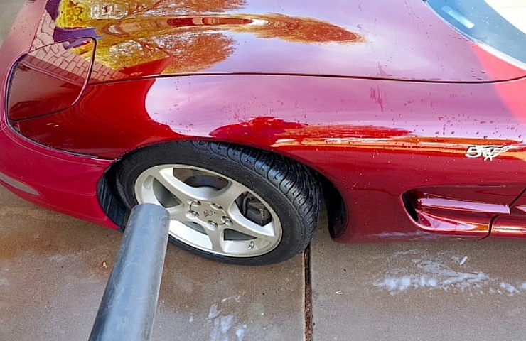 Drying a red Corvette with a leaf blower after washing.