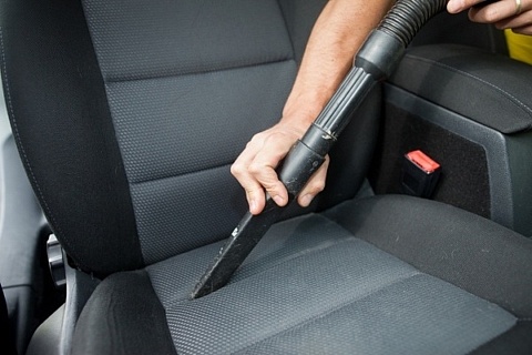 A vehicle owner cleaning a black and gray car seat with a car vacuum.