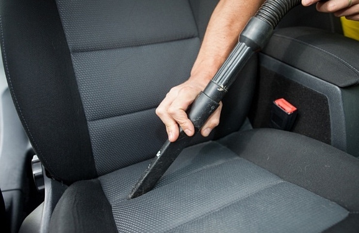 A vehicle owner cleaning a black and gray car seat with a car vacuum.